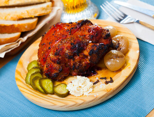Delicious pork knuckle with crispy crust braised in beer served on wooden plate with pickles