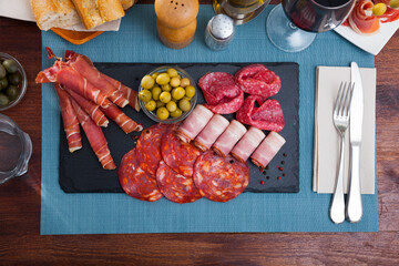 Top view of sliced Spanish dry-cured gammon, chorizo, salami and bacon served with green olives on slate board