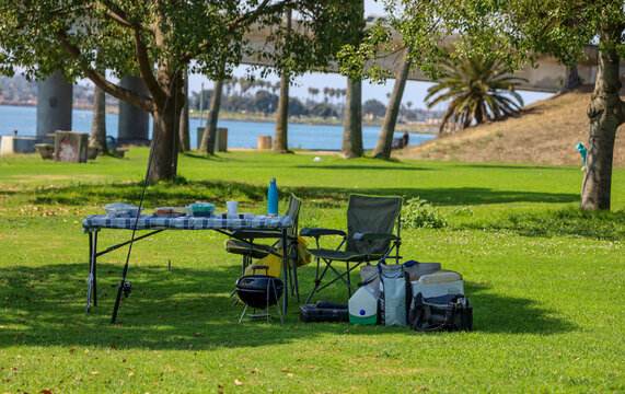 A fishing pole leaning against a picnic table on a grassy area near the water.