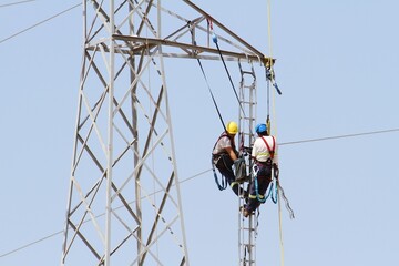 High-voltage tower repair technicians working suspended 20 meters above the ground.