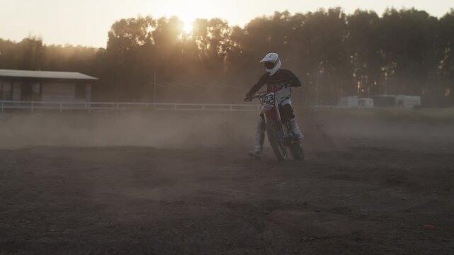 Motorcyclists with protective gear skids on bike raising dust