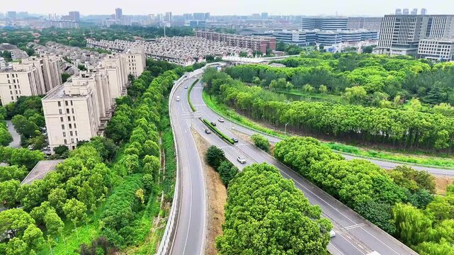 4K UHD aerial drone footage of a city highway surrounded by lush greenery, modern residential buildings, and a toll station, perfect for urban planning, transportation, and travel projects.