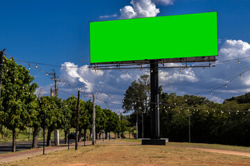 Mockup of the chromakey green billboard under a bright blue sky with white clouds. Outdoor advertising space ready for a message. Simple and clean composition in Brazil