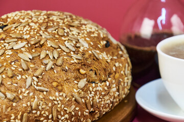 Homemade bread on a wooden board next to a cup of coffee in the foreground with a cherry-colored background
