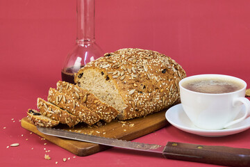 Homemade bread on a wooden board next to a cup of coffee in the foreground with a cherry-colored background