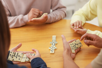 Friends playing dominoes at wooden table, closeup
