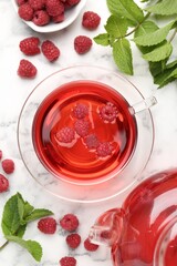 Tasty raspberry tea, berries and leaves on white marble table, flat lay