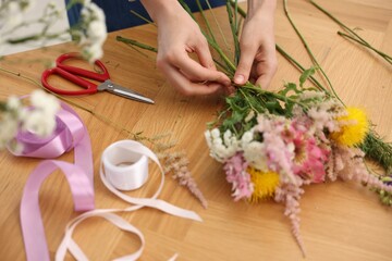 Florist making bouquet of flowers at wooden table, closeup