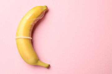 Sex education. Banana with condom on pink background, top view. Space for text