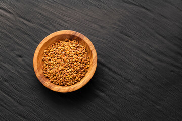 Dried organic fenugreek seeds in the wooden bowl - Trigonella foenum - graecum