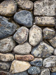 Detailed close-up of a rustic stone wall made with irregularly shaped rocks, showcasing texture and natural colors.