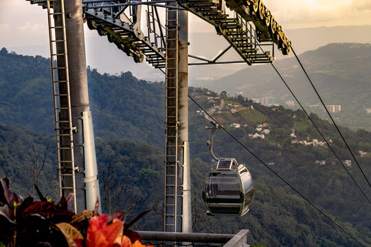 Modern cable car gliding over a mountainous landscape with distant city views, captured at sunset with warm light and scenic hills in the background.