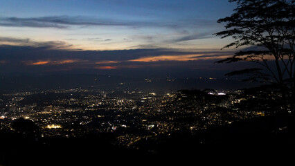 Panoramic view of Bucaramanga, Colombia, illuminated at night under a deep blue twilight sky, framed by silhouettes of trees and fading sunset colors on the horizon
