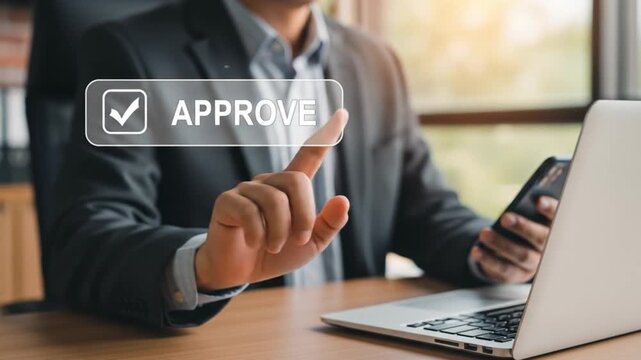 Man using laptop and phone with approve button on screen in office setting for business approval task