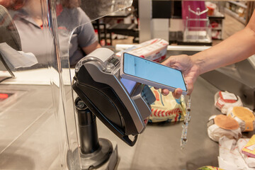 A woman using her mobile phone for contactless payment while holding it over electronic machine....