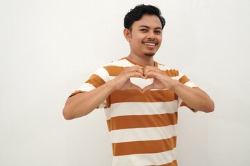 Smiling young Asian man wearing white and brown striped tshirt showing heart gesture, making love...