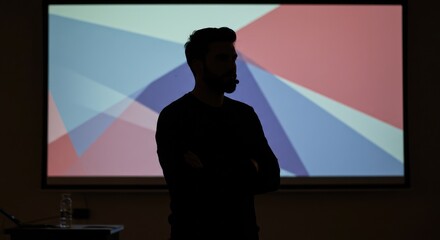 Dynamic speaker presenting ideas confidently with arms crossed before a vibrant abstract geometric projection screen in a modern conference room