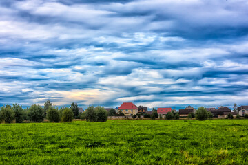 Panoramic view of village houses with colorful roofs located behind a green field. 