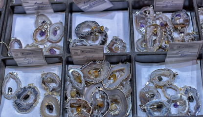 Various pendants made of agate slices with natural crystals inside, neatly laid out in the display case cells.   