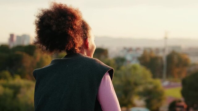 Young woman enjoys the sunset over city landscape. She takes a moment to appreciate the view and golden hour.