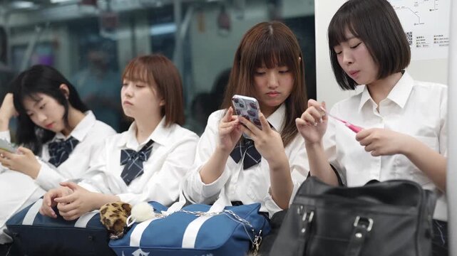 Slow-motion. Japanese high school girls in uniform sit together on a moving train, using smartphones and chatting as the city blurs by beyond window. Shanghai's Pudong New District. China. Spring.