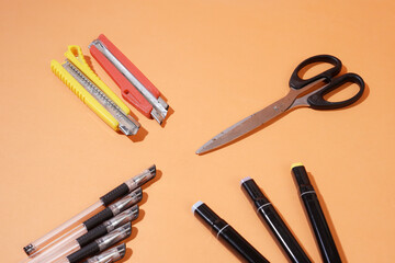 On an orange background, there is a cutter, a highlighter, scissors, and a ballpoint pen
