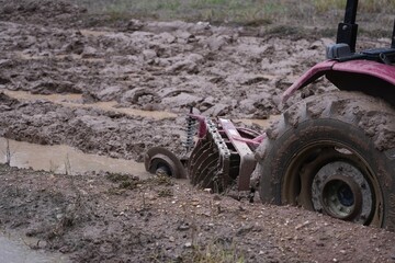 A tractor plowing the muddy and water-filled rice field, preparing the land for cultivation with...