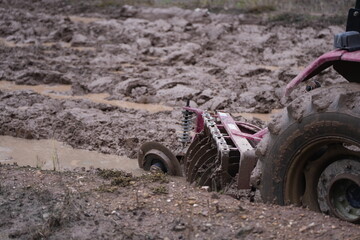 Red tractor working in muddy farmland, plowing and preparing the wet soil for the upcoming rice planting season, representing traditional 