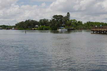 Fototapeta premium Serene Waterfront Scene with Dock, Boat, and Lush Greenery people fishing. Calm mangrove area featuring a dock, a boat, and green vegetation under a partly cloudy sky, conveying tranquility. 