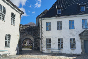 Historic buildings with a stone archway under a blue sky, Bergenhus Fortress in Bergen, Norway
