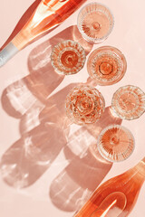 Top view champagne bottle and glasses of rose wine on soft pink background with artistic shadows...