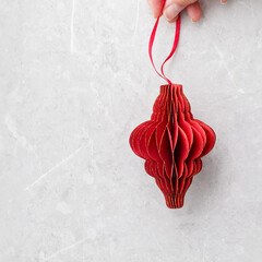 Red Christmas paper bauble as flashlight in woman hand on grey background, Golden Shiny red...