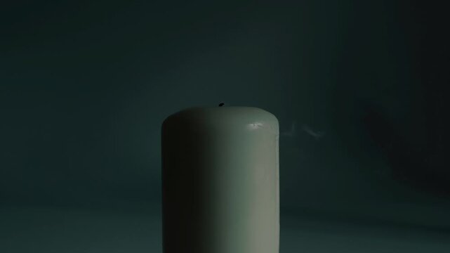A close-up of a candle flame extinguished by a sudden gust of air, leaving a thin trail of smoke on a dark, gloomy background.