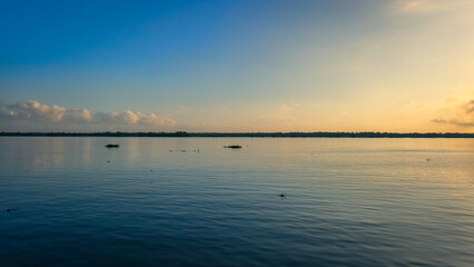 Expansive blue skies reflecting off the calm waters of the Magdalena River at dusk. Clouds add depth and contrast, creating a breathtaking view of nature's beauty in Colombia