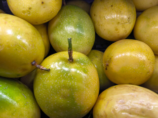 Close-up of fresh yellow passion fruits with speckled skin, stacked together at a market, highlighting their tropical freshness and vibrant color.
