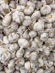 Close-up of fresh garlic bulbs with papery white skin and purple streaks, stacked at a market, showcasing their texture and freshness.