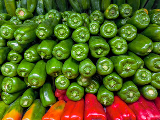 A large pile of green and red peppers are stacked on top of each other. The green peppers are in the middle of the stack and the red peppers are on the bottom. The peppers are fresh and vibrant