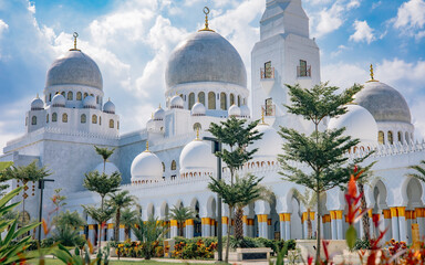 Exterior view of Sheikh Zayed Grand Mosque with domes and minaret under blue sky © Henra