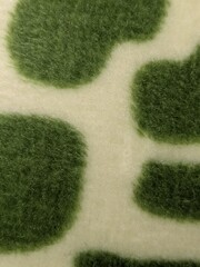 Macro close-up of a soft, fuzzy fabric with a white background and irregular green spots resembling abstract camouflage or giraffe patterns, high detail texture, shallow depth of field, realistic ligh