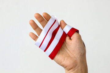 Close-up of a hand holding red and white ribbon with a silver medal, representing achievement,...