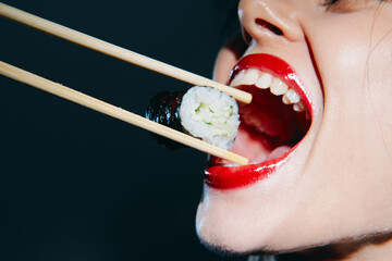 A close-up of a woman's mouth adorned with bright red lipstick, preparing to eat sushi with...
