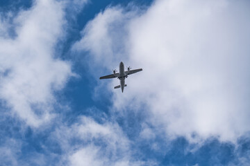 Low-angle view of a turboprop airplane flying overhead against a blue sky with scattered white...