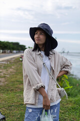 A female traveler dressed in white with a camping hat holding a cup bag, enjoying outdoor adventure in a scenic natural setting.