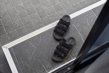 A pair of black flip-flops arranged in front of a house doorway, symbolizing everyday life, simplicity, and homely atmosphere.