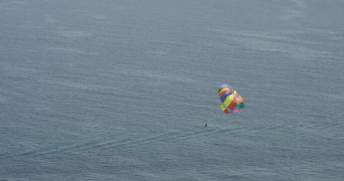 A colorful parasail glides above the Mediterranean Sea, pulled by a motorboat, creating a perfect scene of adventure and summer fun. The vast ocean emphasizes freedom and leisure.