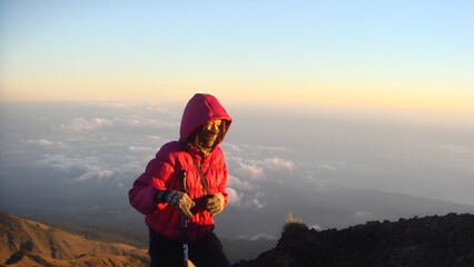 Woman in a red jacket standing on a mountain top above the clouds, perfect for themes of exploration, travel, and outdoor lifestyle
