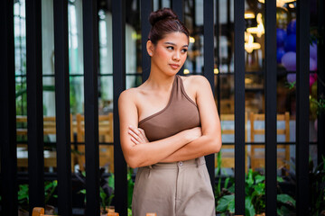 An upset young asian woman standing with her arms crossed and looking to the side, clearly mad and radiating frustration at a cafe.