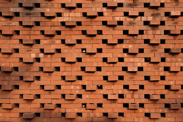 Symmetrical front view of a decorative red brick wall. Geometric architectural background with a perforated pattern, creating a textured and abstract facade.
