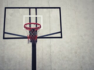A minimalist shot of a basketball hoop against a textured, weathered concrete wall. The hoop, with...