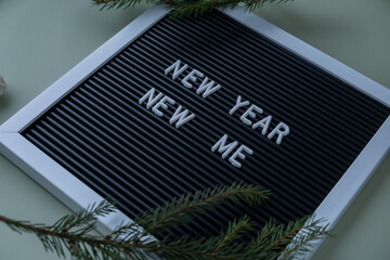 NEW YEAR NEW ME text on black letter board on green background with Christmas decor. New year aims...